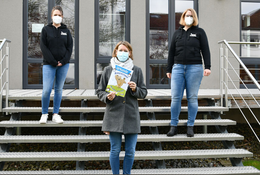 Petra Huppert Buch, Silke Merkel und Sandra Wegener stehen auf einer Treppe und zeigen eine Urkunde vom Programm 'Bärenstark'.