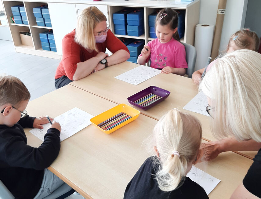 Vorschulkinde sitzen mit Lehrerinnen an einem Tisch und lösen Aufgaben.