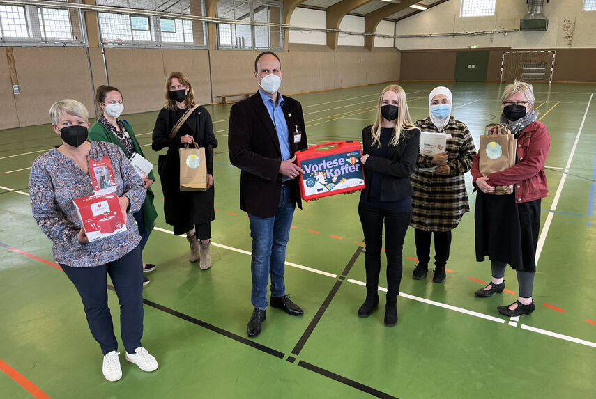 6 Personen halten in einer Turnhalle den Vorlesekoffer in den Händen.